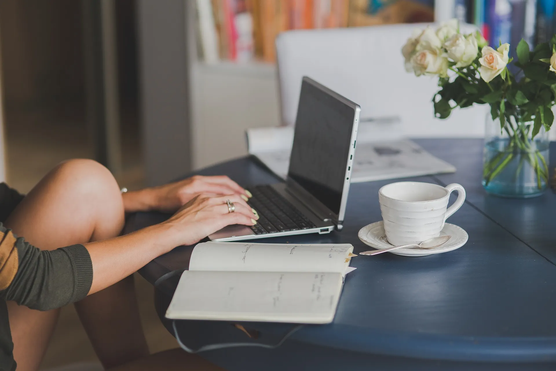 Close-up of a person working remotely, typing on a laptop with a notebook and coffee on a table.